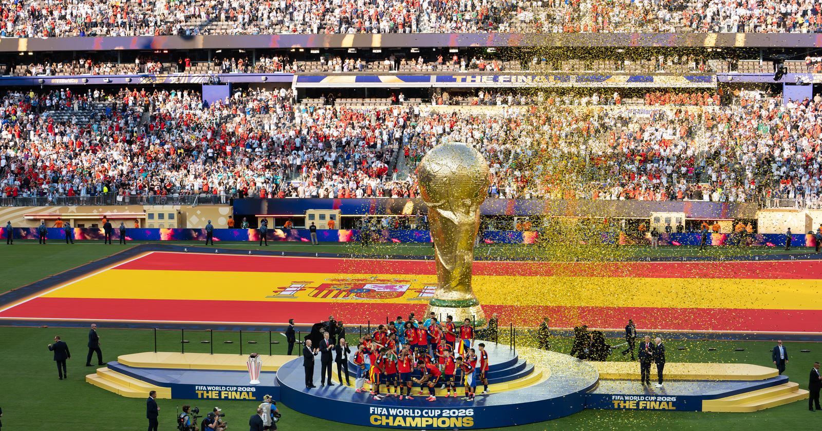 Prisutdelningen efter VM-finalen 2026 med en jättelik VM-pokal, Spaniens flagga över planen och guldkonfetti